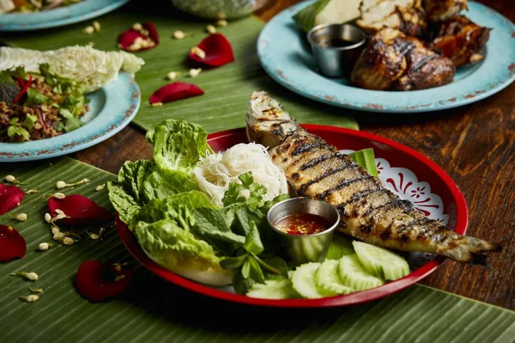 Grilled whole seabass with vegetables and noodles in red tray on banana leaves