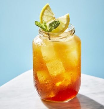 Boozy Thai iced tea with lemon and mint garnish on pastel blue background