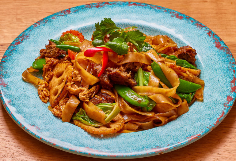 StirfryFlatNoodlesVeg Stir fry flat noodles with vegetable in a blue plate on a wooden table